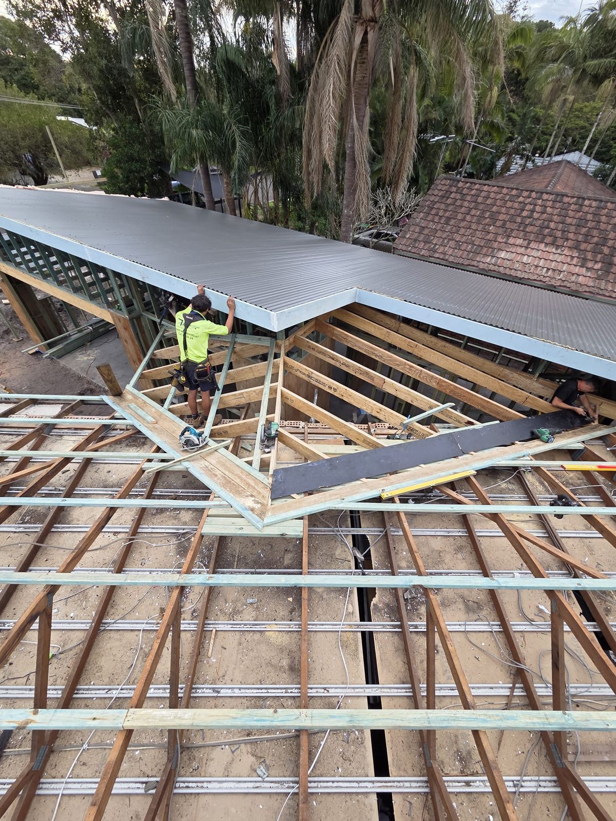 Worker fixing metal roof sheets over timber framing